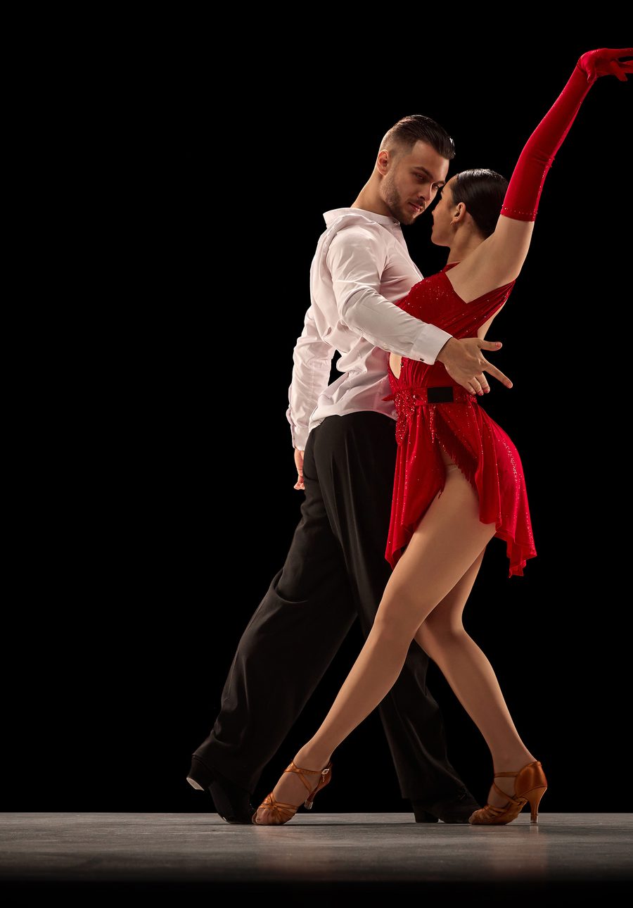 A couple in a dramatic pose on a dark stage, the woman in a red dress and long red gloves