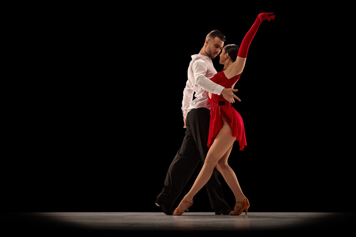 A couple in a dramatic pose on a dark stage, the woman in a red dress and long red gloves