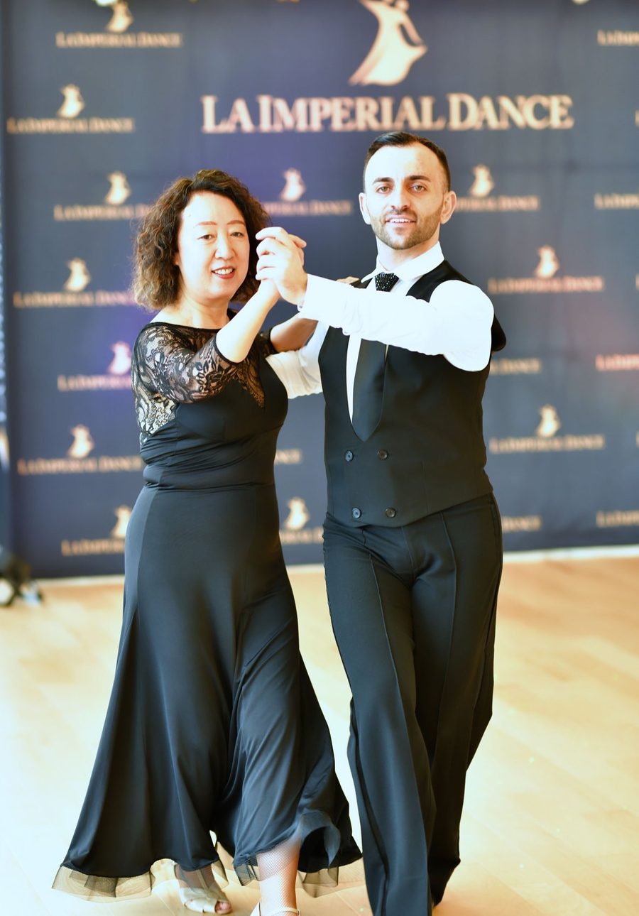 Vard Margaryan and a student in a long black gown dancing in hold in front of the studio’s La Imperial Dance banner