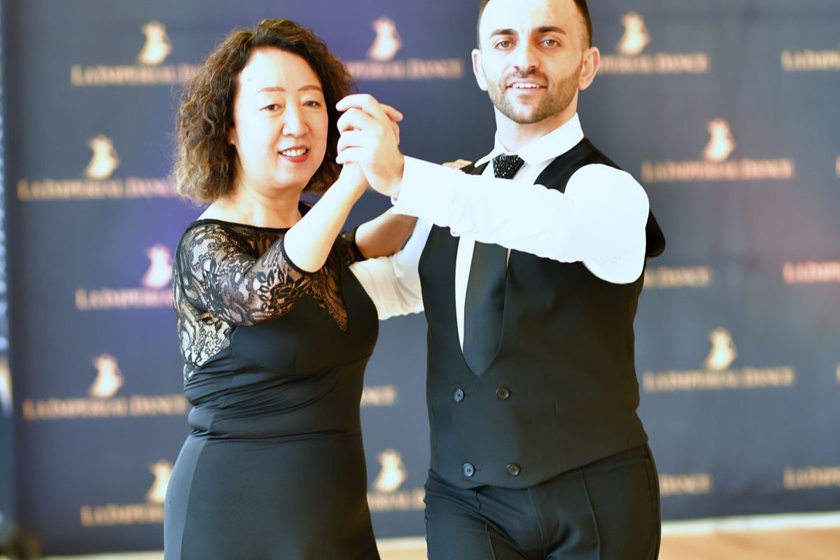 Vard Margaryan and a student in a long black gown dancing in hold in front of the studio’s La Imperial Dance banner