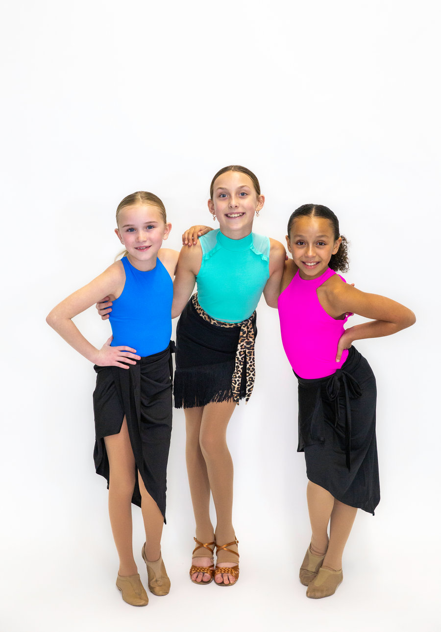 Three young dancers in Latin practice costumes, arm in arm and smiling