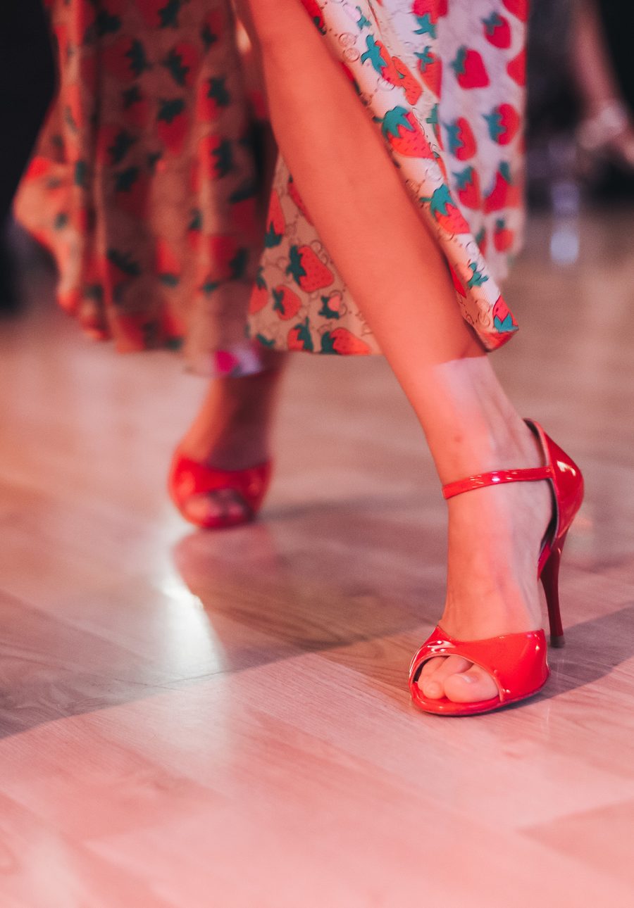 Close view of a couple dancing at a party, the woman in red strappy heels and a strawberry-print dress