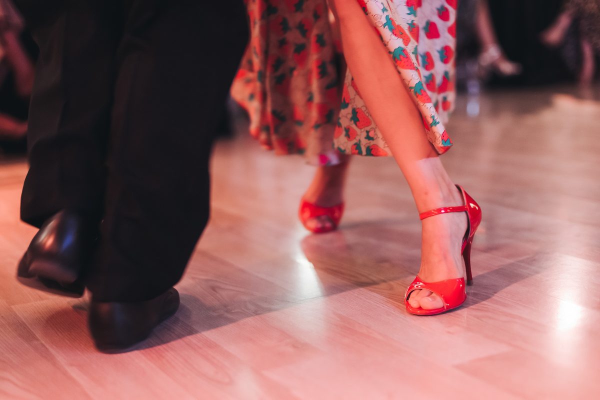 Close view of a couple dancing at a party, the woman in red strappy heels and a strawberry-print dress