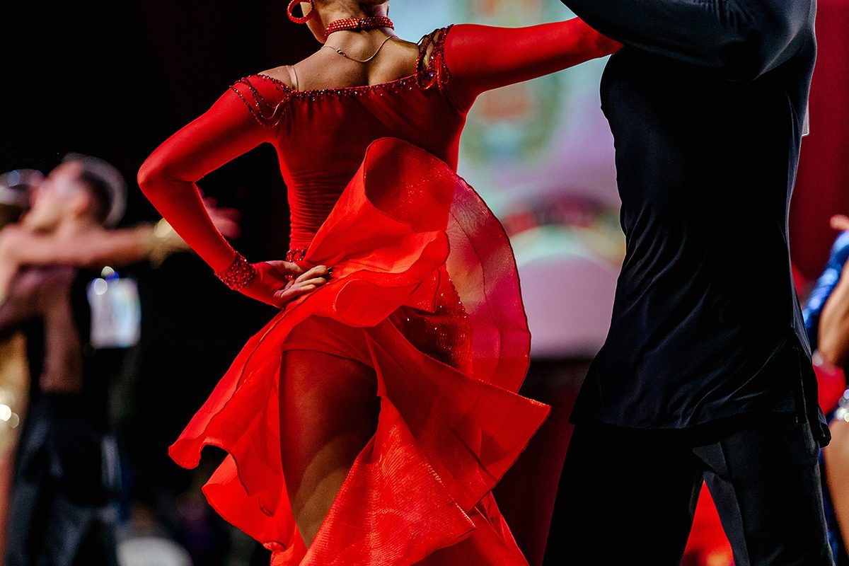 A dancer in a flowing red dress with her hands on her hips, swirling the skirt like a cape