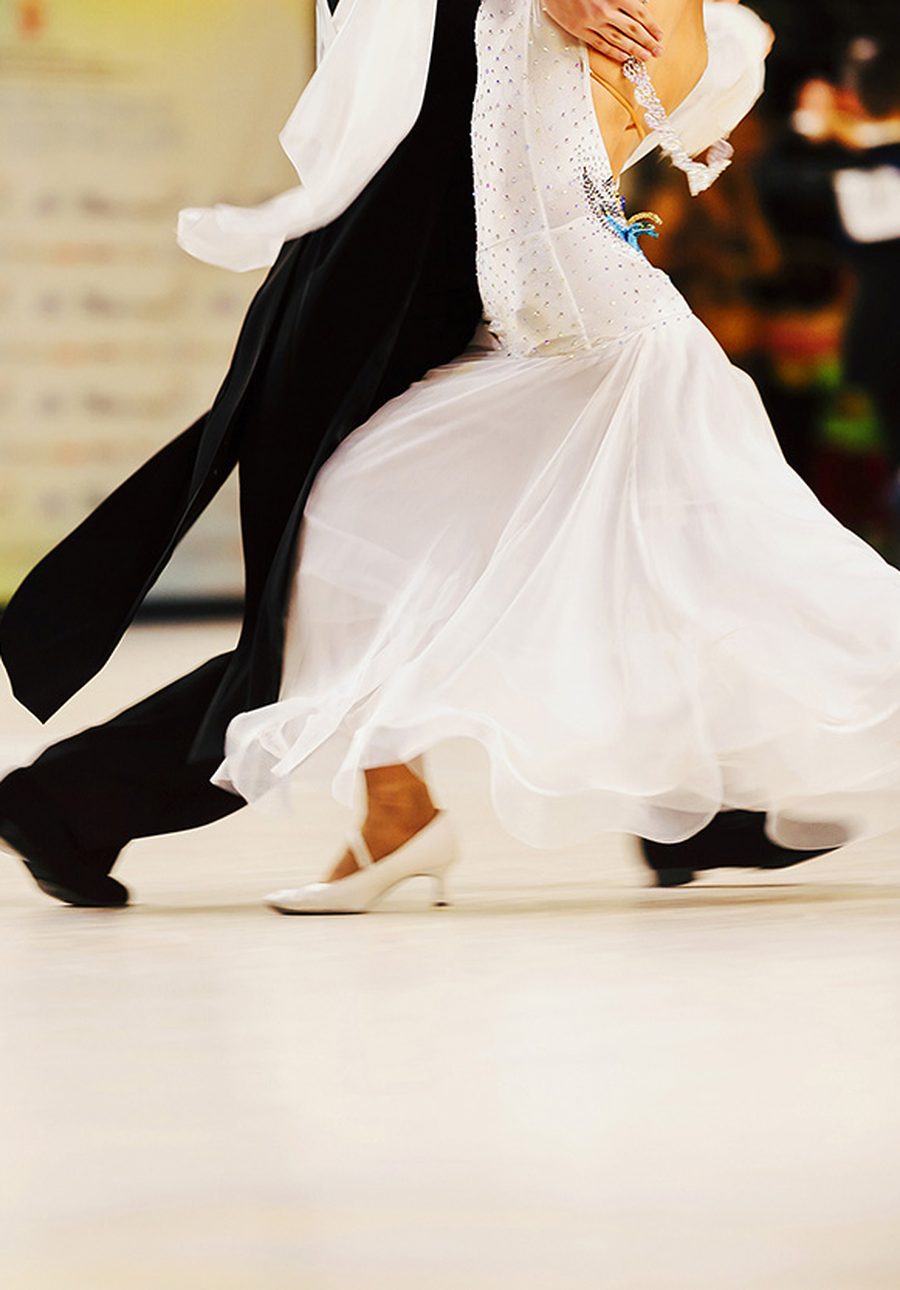 A ballroom couple travelling across a competition floor, the woman in a flowing white gown