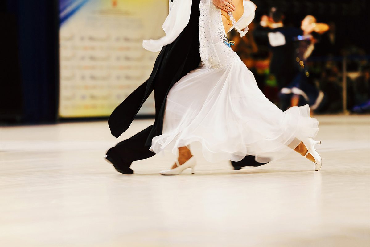 A ballroom couple travelling across a competition floor, the woman in a flowing white gown