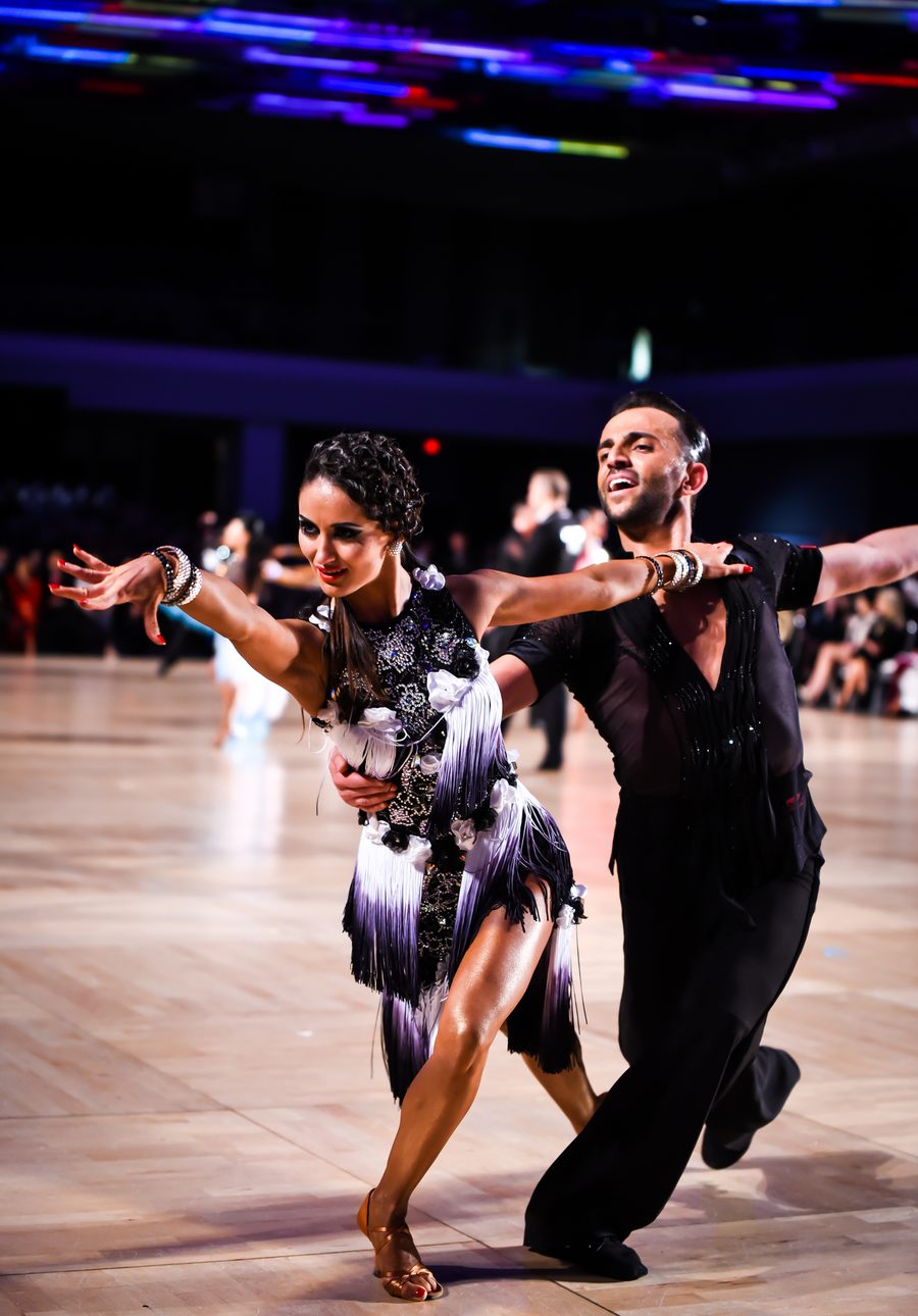 Vard Margaryan and his partner in a Latin pose on a competition floor, she in a black and white fringed dress