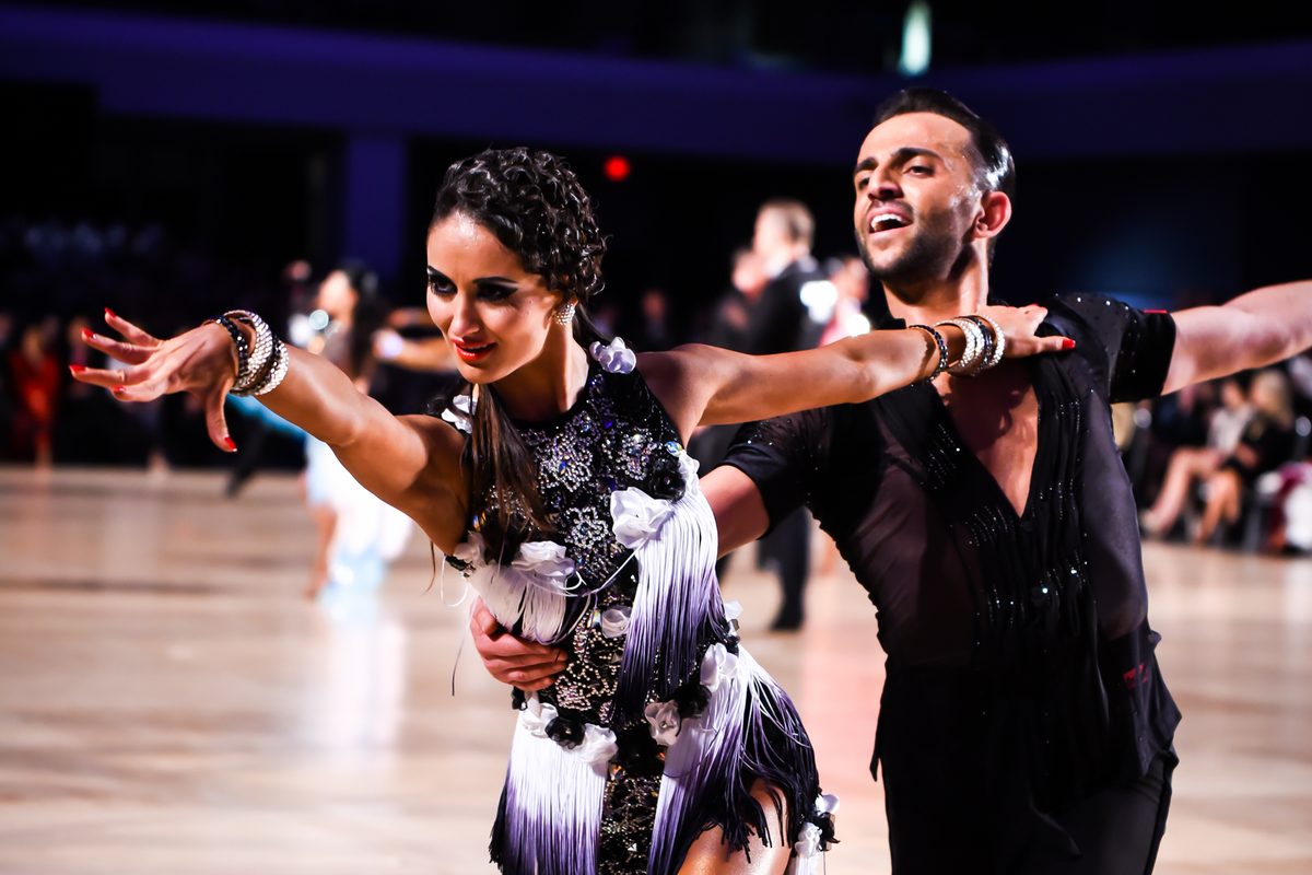 Vard Margaryan and his partner in a Latin pose on a competition floor, she in a black and white fringed dress