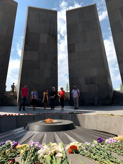 Six of the group standing between the memorial's tall stone slabs, above the eternal flame