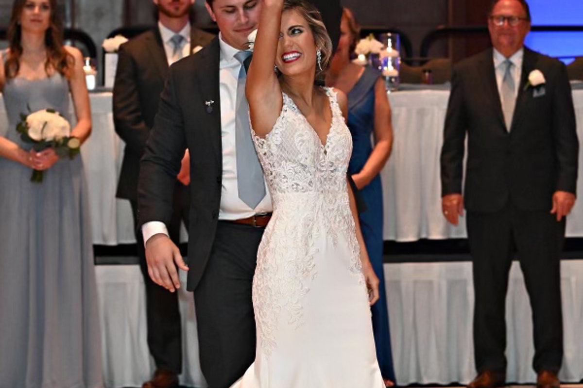 A groom turning his bride under his arm on the dance floor as the wedding party looks on