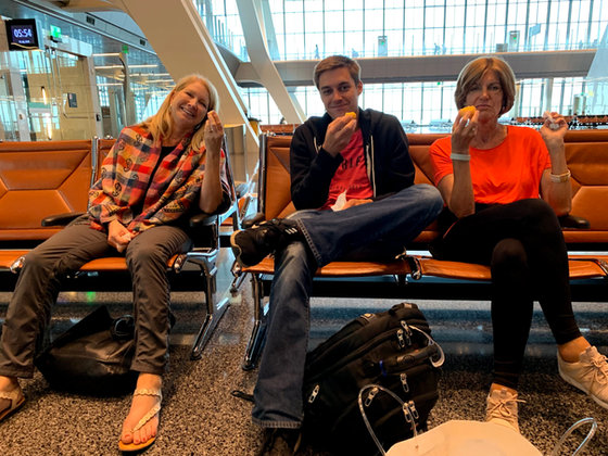 Three of the group waiting in the departure lounge, each holding a piece of fruit