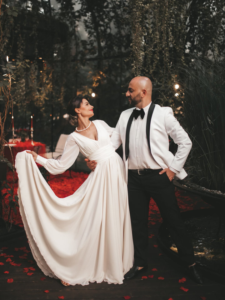 A couple in evening dress standing among scattered rose petals at an evening celebration