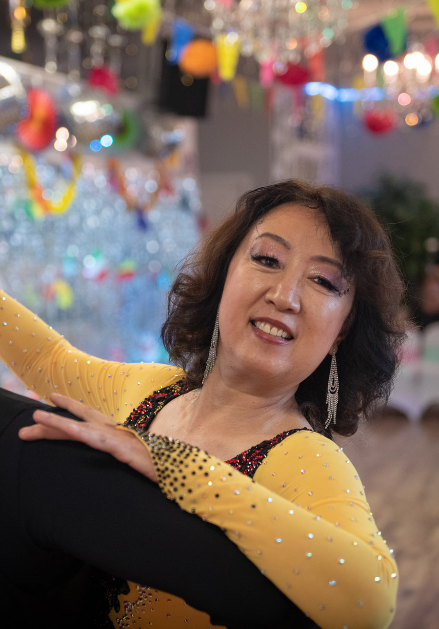 A student in a gold gown smiling as she dances with her instructor at a VM Ballroom party