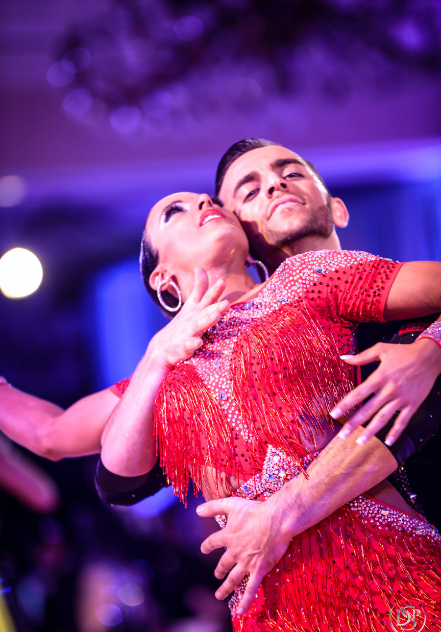 A couple dancing Latin in a red fringed costume on a competition floor
