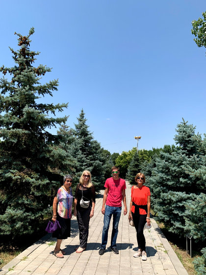 Four of the group on a paved path between tall blue spruce trees