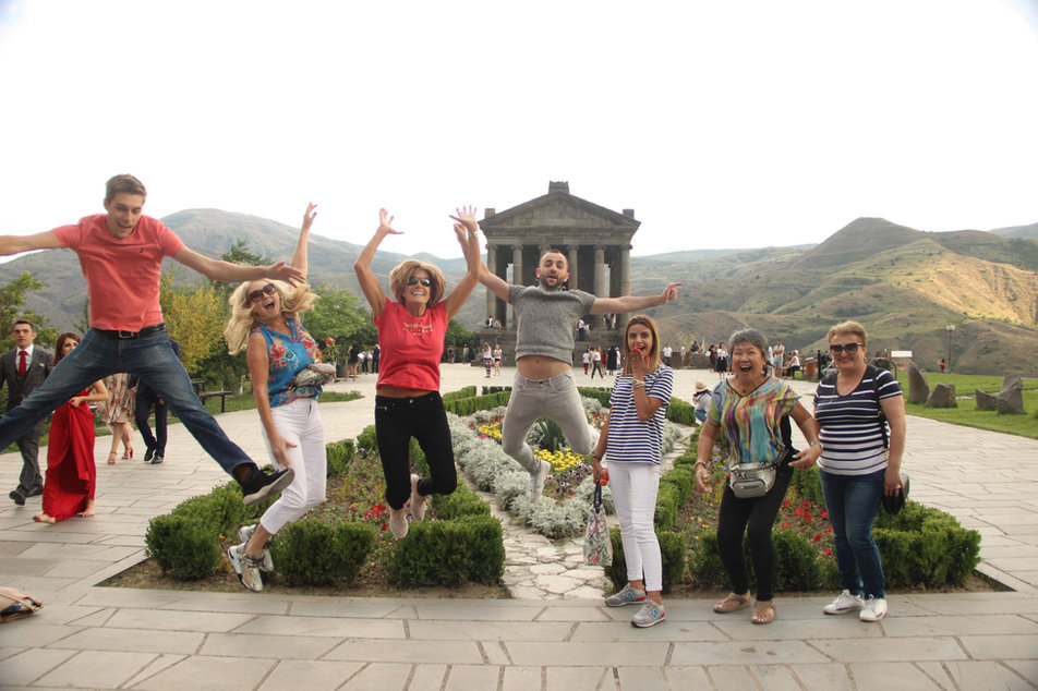 The group jumping in the air in front of a colonnaded stone temple on a hillside