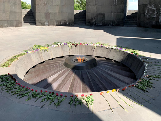 Carnations laid all around the sloping stone rim of the memorial, close to the flame