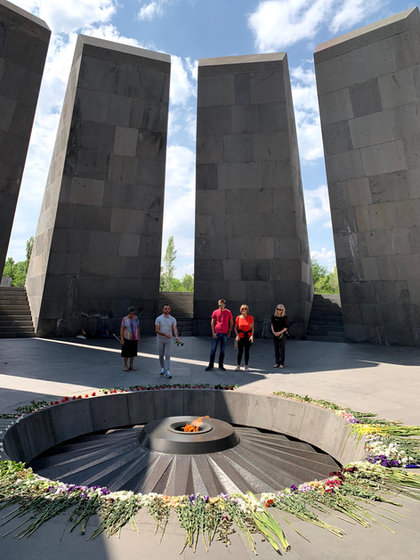 Five of the group standing in a stone plaza behind a circular memorial, its eternal flame ringed with flowers