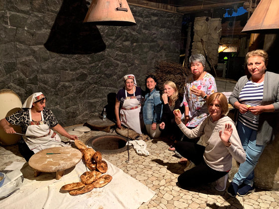 A baker in an apron and headscarf lifting flatbread from a stone oven while the group watches