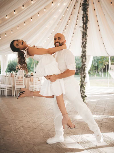 A couple dressed in white dancing together beneath a draped marquee