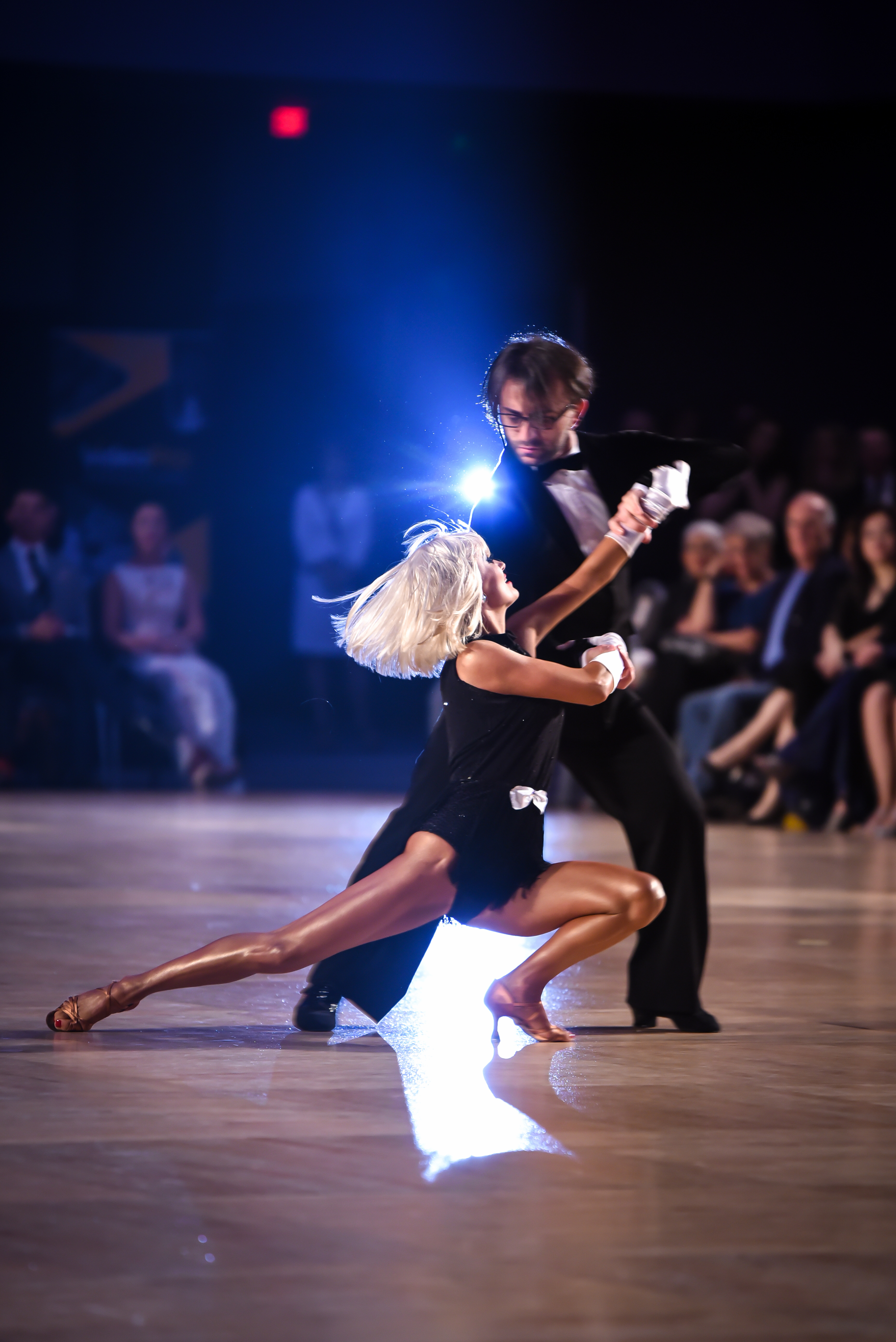 A couple dancing a Latin routine under a spotlight on a competition floor