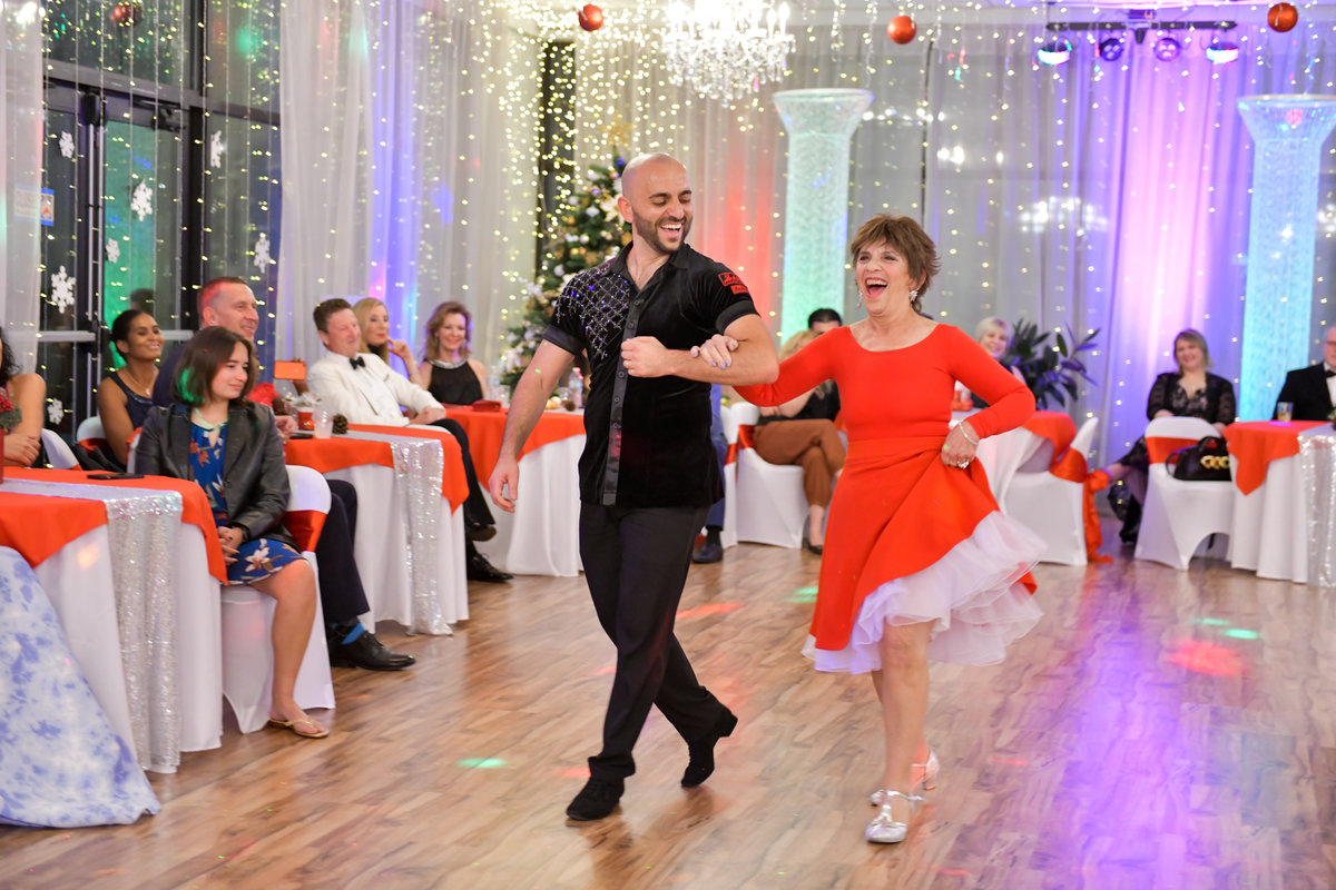 A student and her instructor dancing in front of seated guests at a VM Ballroom Dance Studios party