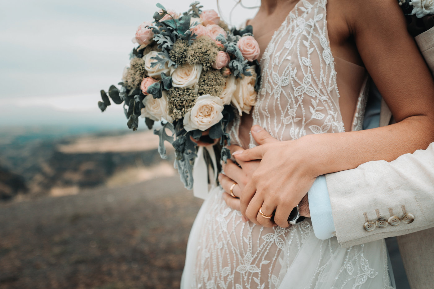 A bride holding her bouquet with her groom’s arms around her