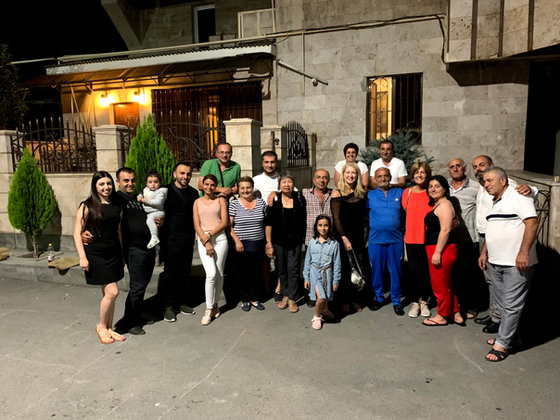 Travellers, hosts and children together outside a house in the evening