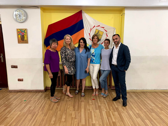 Six of the group standing in a hall in front of the Armenian flag