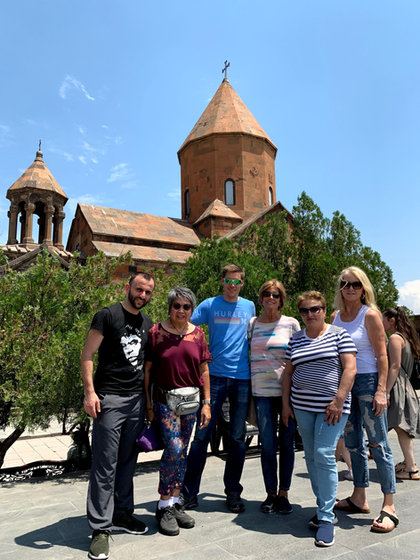 Six of the travelling party in front of a red-stone Armenian church with a bell tower