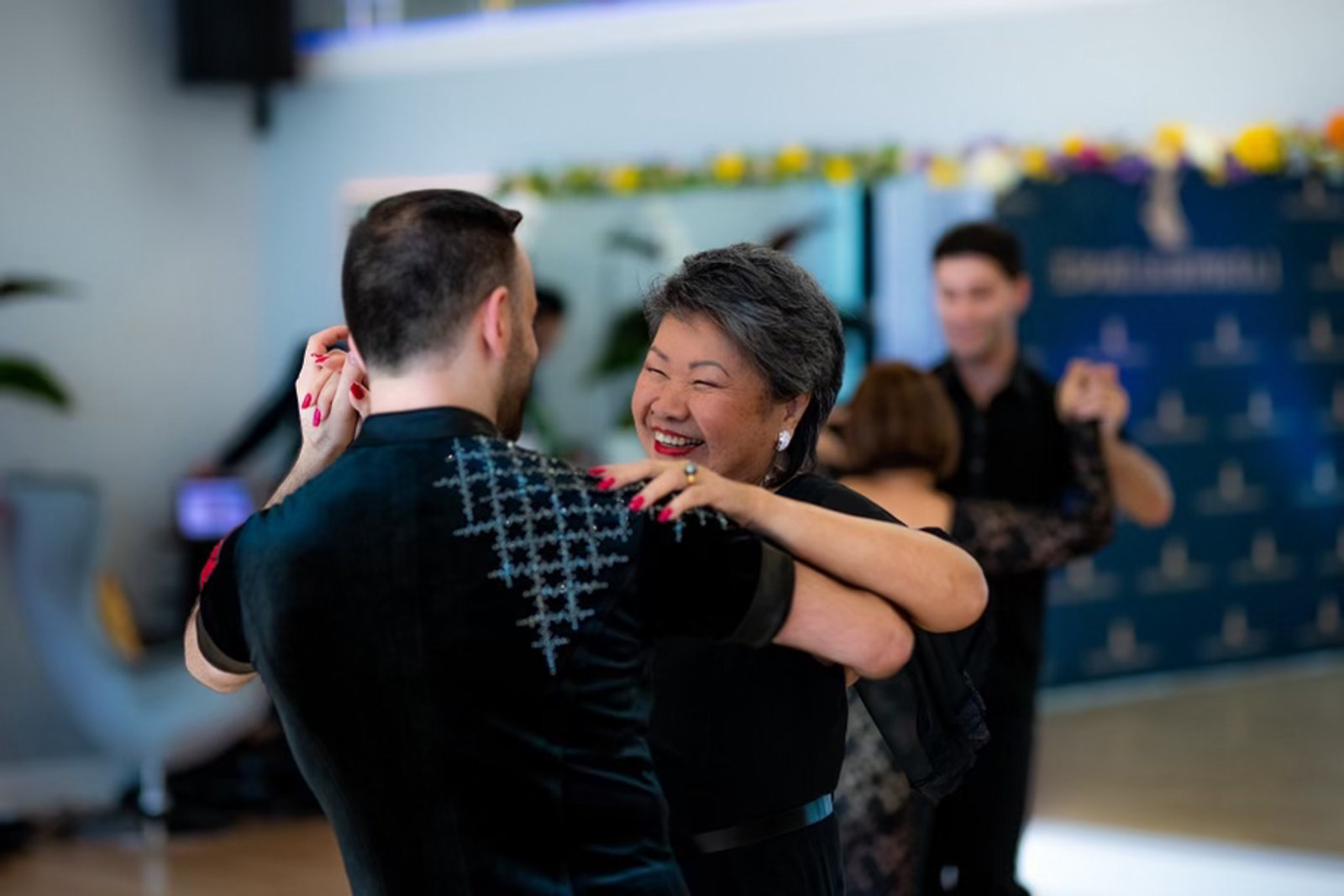 Two dancers smiling in a close hold on the floor at a VM Ballroom Dance Studios event