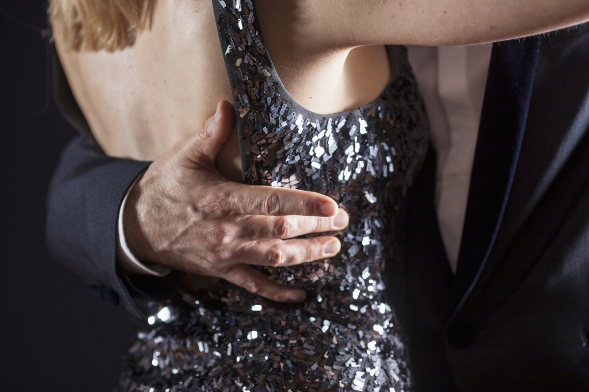 A close view of a dancer’s hand on the back of a partner’s sequinned gown in a closed hold