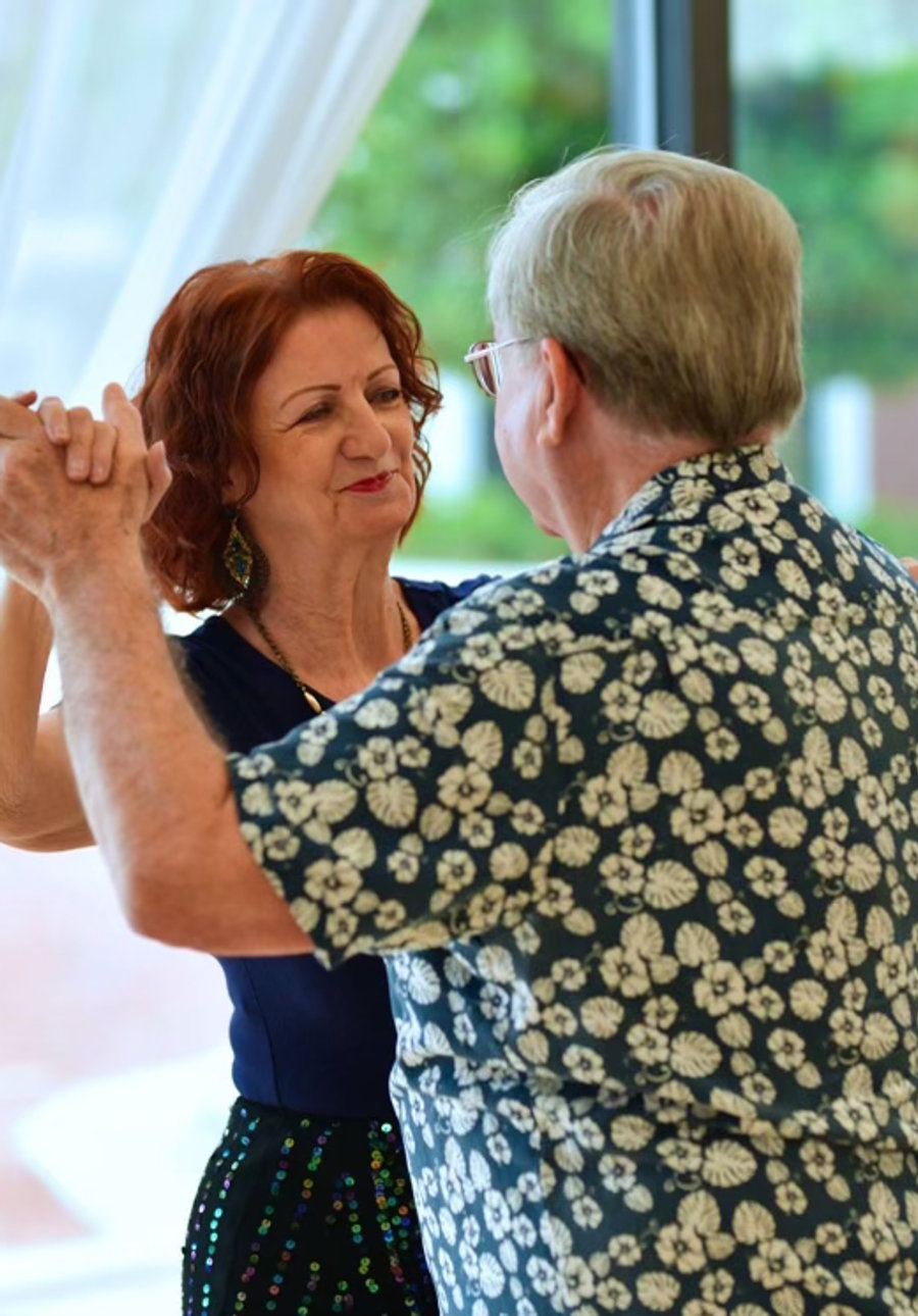 A smiling couple dancing in a closed hold beside the studio windows at VM Ballroom Dance Studios